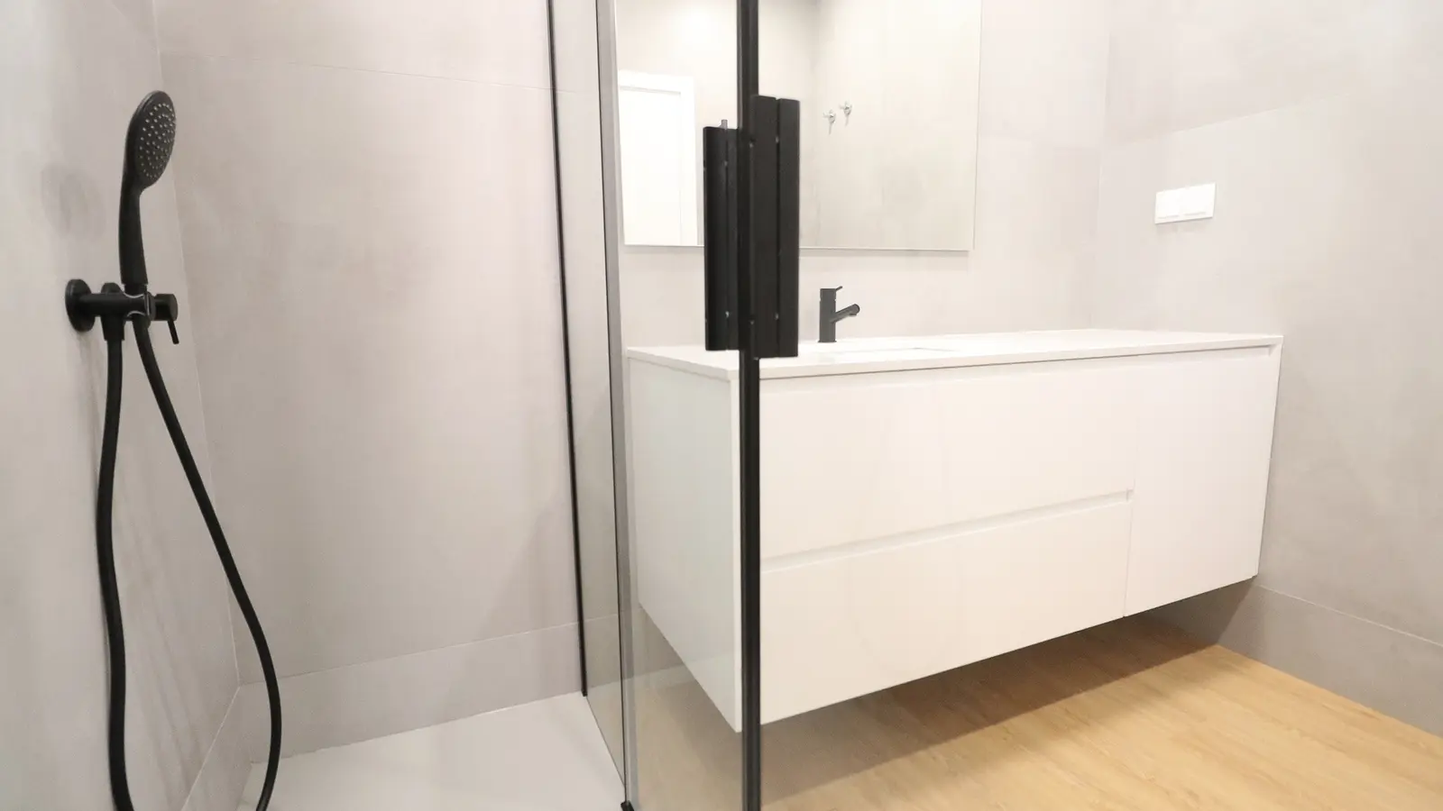 Baño claro con ducha de vidrio, paredes grises, mueble blanco suspendido y grifería negra