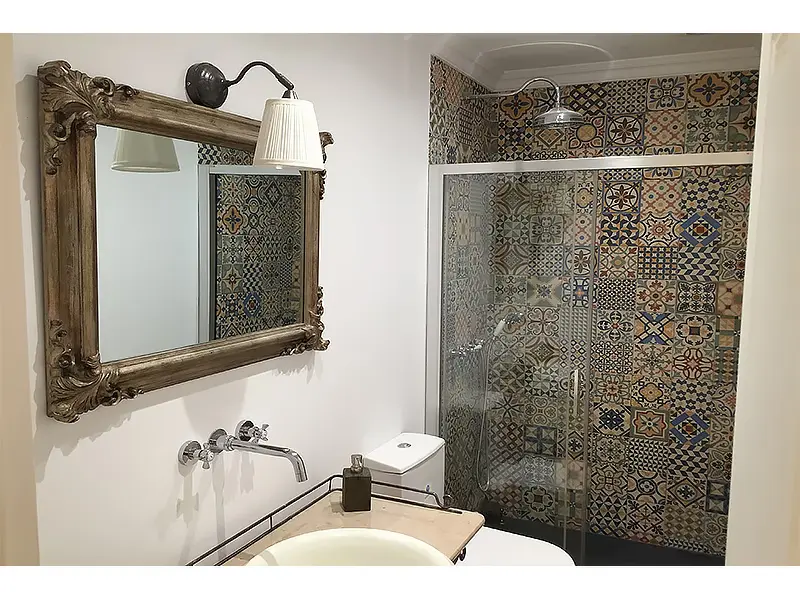 Baño con ducha de vidrio, azulejos de motivos variados y espejo de marco tallado