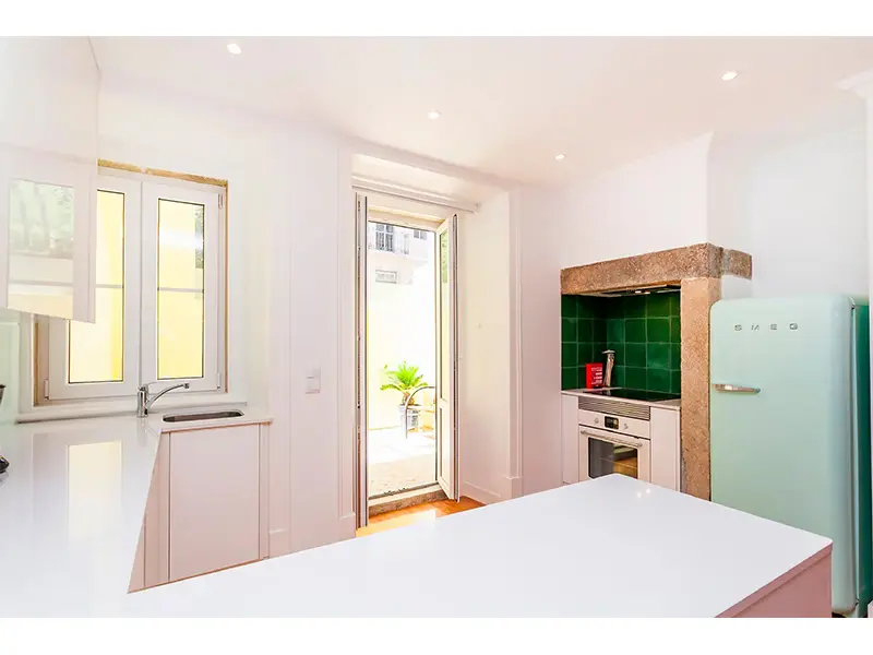 Cocina blanca con isla, frigorífico verde agua y frente verde bajo una campana de piedra